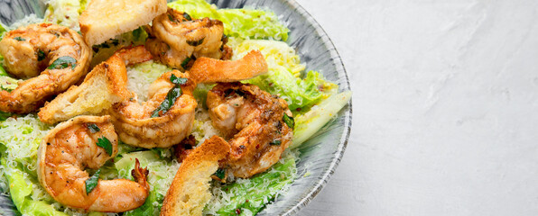Classic caesar salad with grilled shrimps on gray background.