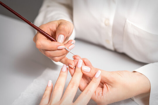 French manicure. Manicure master drawing white varnish on the nail tip with a thin brush, close up