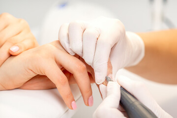 Obraz na płótnie Canvas Manicure master applying electric nail file machine removing old nail polish on fingernails in a nail salon