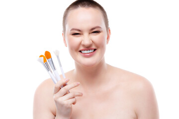 Short-haired woman with bare shoulders showing make-up brushes set against white background