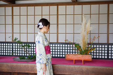 Young Japanese woman in kimono looking at ikebana flower arrangements
