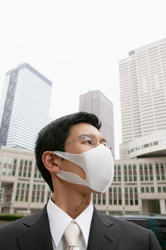 Portrait businessman in face mask below city highrise buildings
