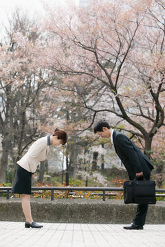 Japanese business people bowing to each other in park
