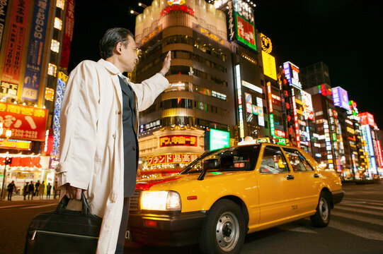 Businessman hailing taxi on city street, Tokyo, Shinjuku, Japan
