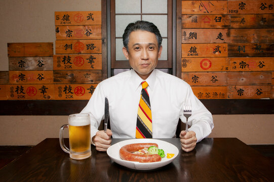 Portrait hungry businessman with sausage and beer in restaurant
