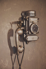 Old vintage wired telephone for communication hangs on textured gray wall. Antique phone from past for background. History of telephone in world. Concept of communications and telegraph. Copy space