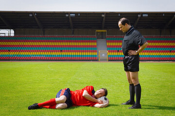 Soccer coach watching player sleeping on ball on sunny pitch