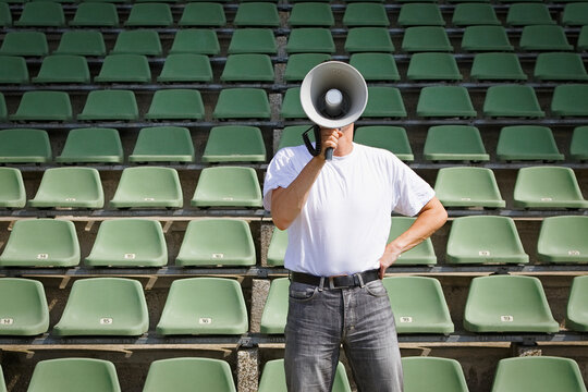 Man using bullhorn among green stadium seats
