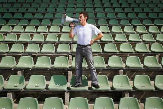 Man yelling into bullhorn on green stadium seats
