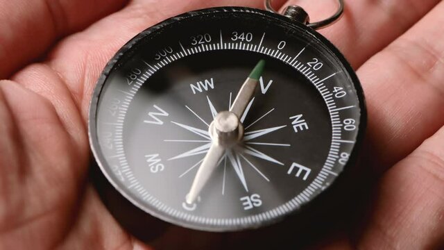 Male hand holding a compass with a green arrow that shows the direction. Concept of travel, adventure, expedition, business, choice and possibilities.