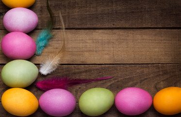 bright Easter eggs on the background of a wooden table with feathers with a copy of the space