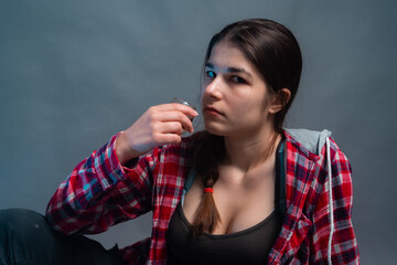 A girl sits on a gray background and drinks alcohol from a glass.