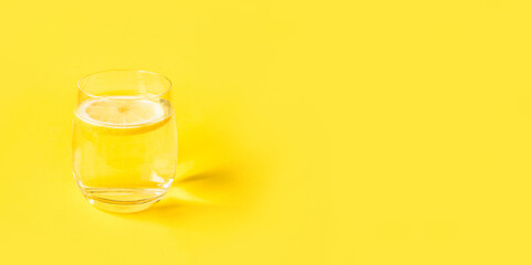 Glass of water with lemon on a yellow background. Summer refreshing drink.