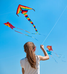 The little girl in the t-shirt plays on the beach by the sea with a colorful kite. In the background many people are walking on the beach.