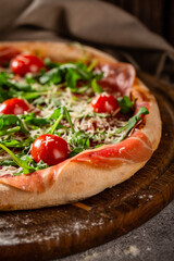 Pizza close up with arugula, prosciutto and cherry tomatoes on a wooden board.