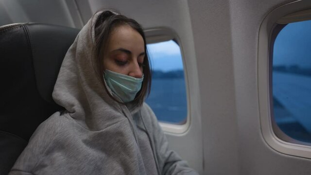 woman in hoodie and medical mask in airplane cabin. travel and air flights during Covid-19 pandemic and quarantine. new life and norms in post pandemic world