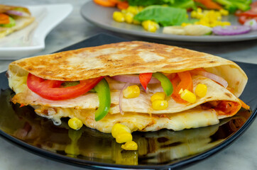 Closeup of delicious Tortilla Wrap Sandwich with vegetables and cheese in a black plate