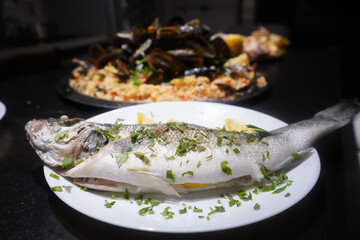 Sea perch perched on a white plate with parsley and lemon, only good to put in the oven. Product photography.