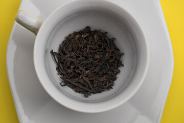 White teacup with black tea inside on a yellow background