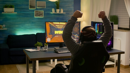 Videogamer player raising hands after winning first person shooter competition wearing hradphones. Professional pro gamer playing online video games with new graphics on powerful computer © DC Studio