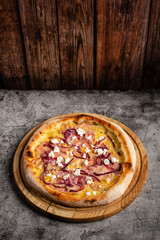 Pizza with ham, cheese and cottage cheese lies on a wooden board.