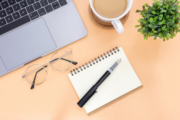 Top view workspace with coffee cup , notebook, pen and laptop copy space on orange color background