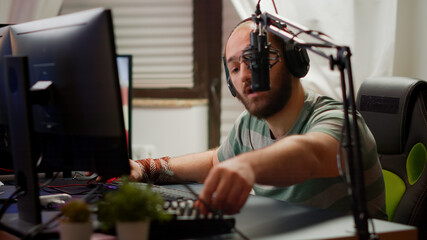 Professional man streamer preparing for virtual gaming tournament checking sound mixer playing from home studio at RGB powerful computer. Cyber gamer performing at online esport championship