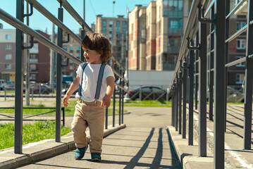 Long-haired cute toddler boy walking along the ramp outdoors of the city street