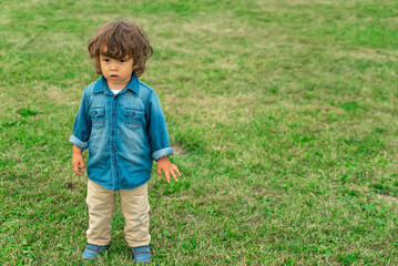 Long haired cute little boy standing on the lawn outdoors.