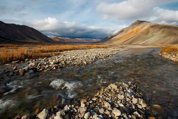 Autumn Arctic landscape. View of a small river in the tundra. In the distance, a lake and...