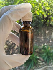 A man who wears a white glove is holdings non labelled vaccine bottle with blurred on background at the garden