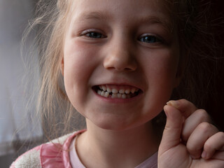 Cute preschooler child wobbling her lower milk tooth and smiling. Deciduous tooth replacement by...