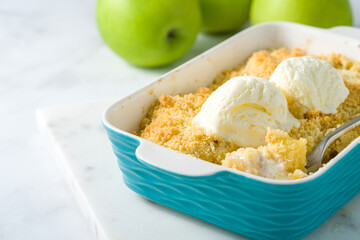 Apple and pear crumble with ice cream, streusel. Sweet dessert with stewed fruit topped crisp crumbly mixture. Apple cobbler pie in blue baking dish on white table. Side view, copy space