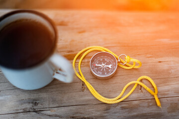 a tourist compass on a yellow rope lies on a log next to a mug of tea, as a hiking and travel concept.