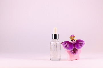 Obraz na płótnie Canvas Glass cosmetic bottle with serum for skin care and orchid flower on a light background. Copy space