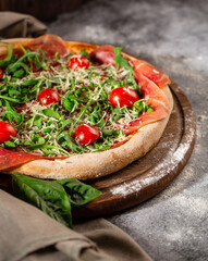 Traditional New York style pizza with prosciutto arugula and cherry tomatoes.