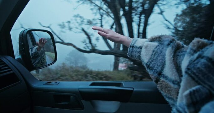 Cinematic shot of young woman drive on passenger seat of camping van, travel on road trip. Moody autumn day, inspiring wanderlust travel blogger concept. Move hand in wind, enjoy adventure and nature