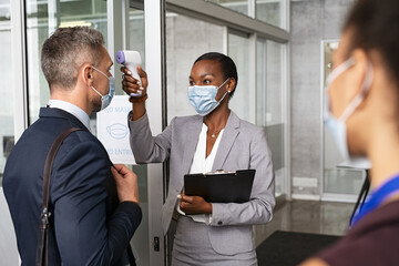 Businesswoman using infrared thermometer before letting people into the office - Powered by Adobe