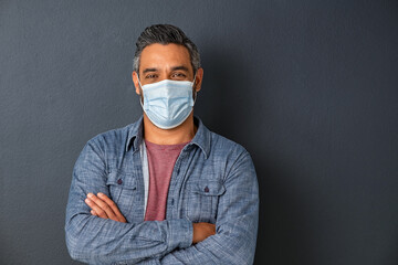 Happy middle eastern man wearing protective face mask on grey wall with copy space