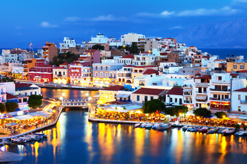 Fototapeta na wymiar Beautiful southern town of Agios Nikolaos at summer evening. Boats swing on the water of the lake Voulismeni at the pier with evening lights. Crete Island. Greece