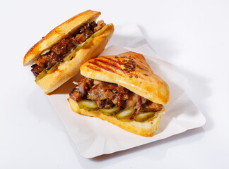 Hot sandwich with meat and pickled cucumber on a disposable paper plate. White background. Side view.