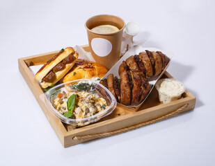 Delicious lunch with disposable tableware on wooden tray. Lemon tea, salad, baked potatoes with meat, sauce and buns.