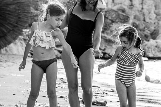 A young mother and her two little daughters on the seashore are looking at something in the sand.