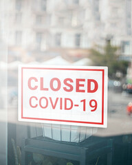 Close up on closed sign in the window of a shop with inscription Closed due to Covid-19. Stores, restaurants, offices, other public places temporarily closed