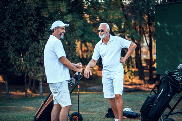 Two older men stand on a golf course and talking. - 423158721