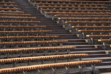 Lots of wooden rounded benches in an empty amphitheater outside in the sunshine by day 