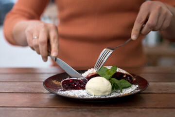 Woman cuts vegetarian dessert, cherry strudel on wooden table