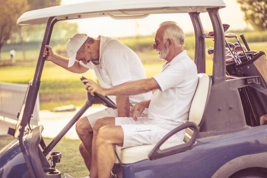 Two happy older friends are riding in a golf cart.