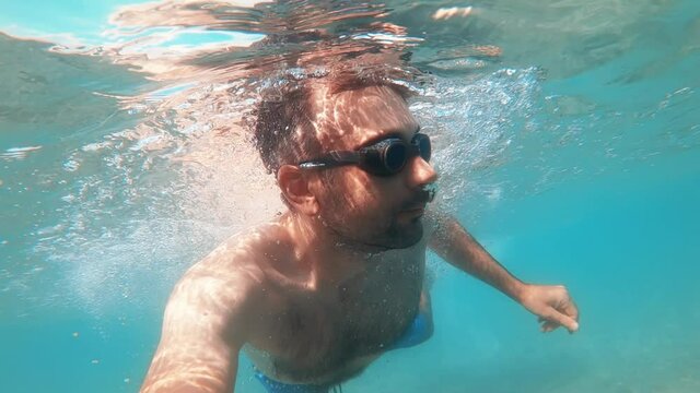 Man in swimming goggles under the water and holding camera, Aegean sea. Slow motion, underwater shooting. Greece