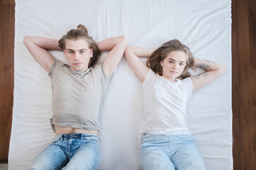 Young attractive heterosexual couple man and woman lie on the bed in the bedroom dressed in casual clothes. Weekend rest in bed is a good time